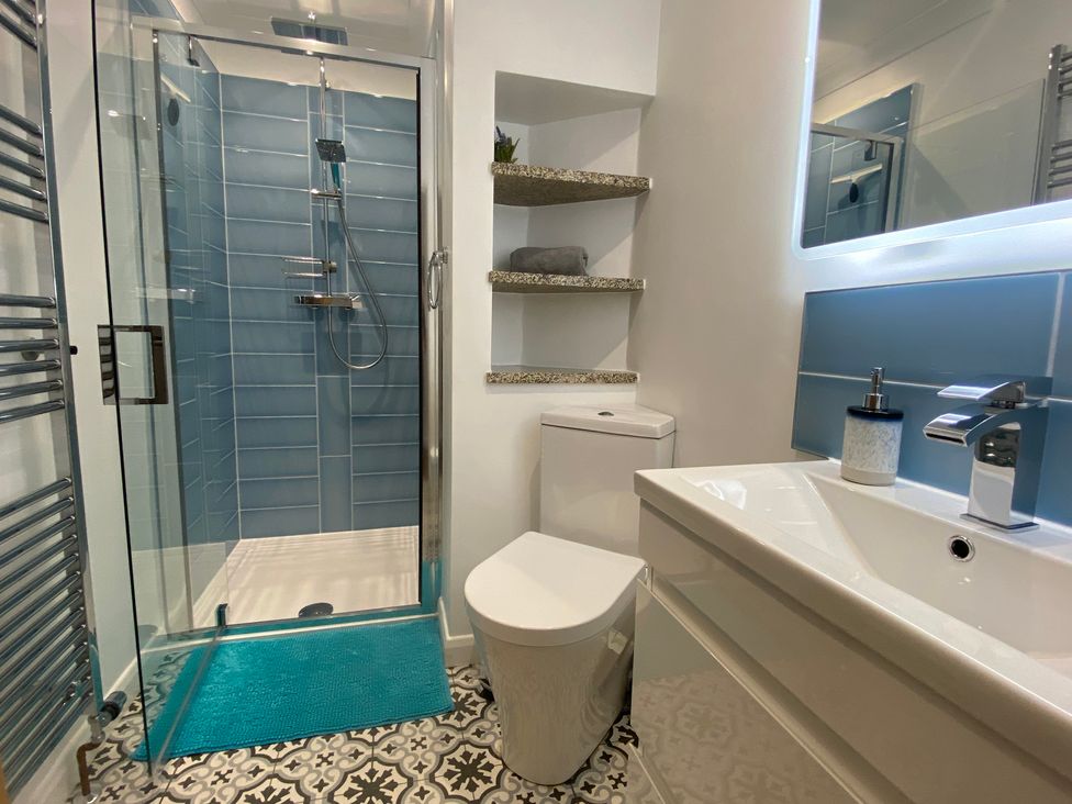 A bathroom with a glass shower, toilet, sink, shelves, and patterned floor tiles at Ashlea in Launceston