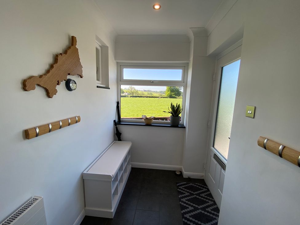 A small entryway with a window showing a green field a white bench with compartments a wooden wall map a clock and coat hooks at Ashlea in Launceston