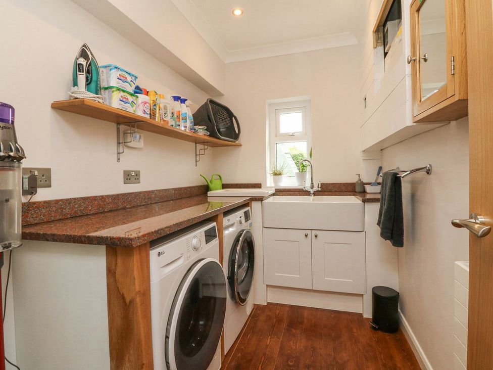 A laundry room with washer and dryer under a countertop and a sink by a small window at Ashlea in Launceston