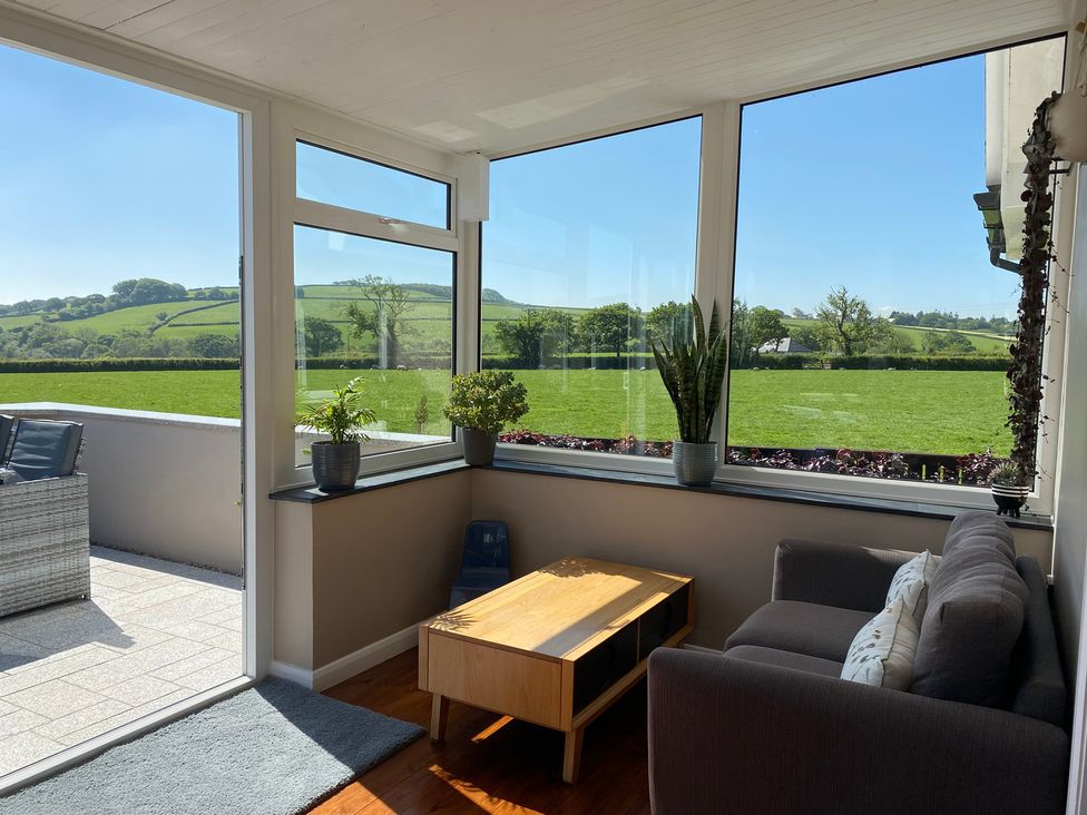 A sunroom with large windows overlooking green fields furnished with a gray sofa wooden coffee table and potted plants at Ashlea in Launceston