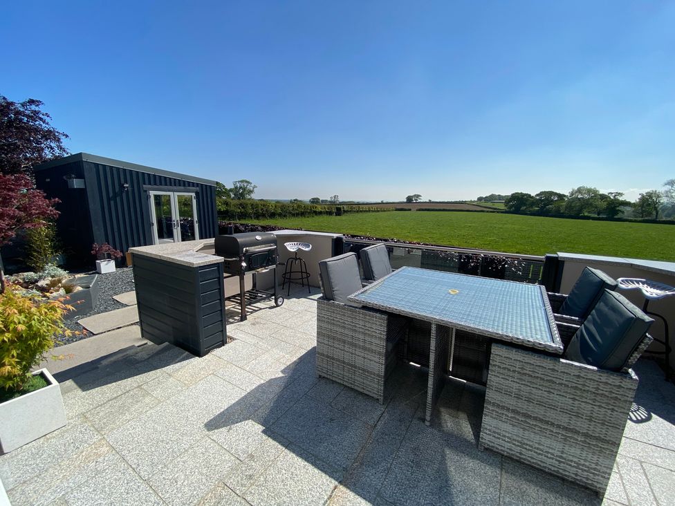 An outdoor patio with a table and chairs a barbecue grill raised counter and a small building with glass doors overlooking a grassy field at Ashlea in Launceston