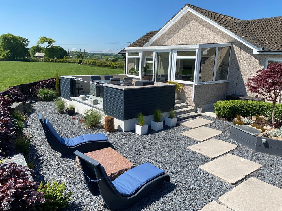 A garden patio with blue cushioned loungers a stone table and a raised dining area outside a house at Ashlea in Launceston