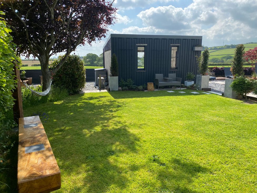 A garden with a lawn tree a wooden bench a hammock a black shed with two windows and outdoor chairs at Ashlea in Launceston