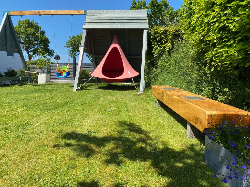 A garden with a children's swing, a hanging chair, a wooden bench, and green grass at Ashlea in Launceston