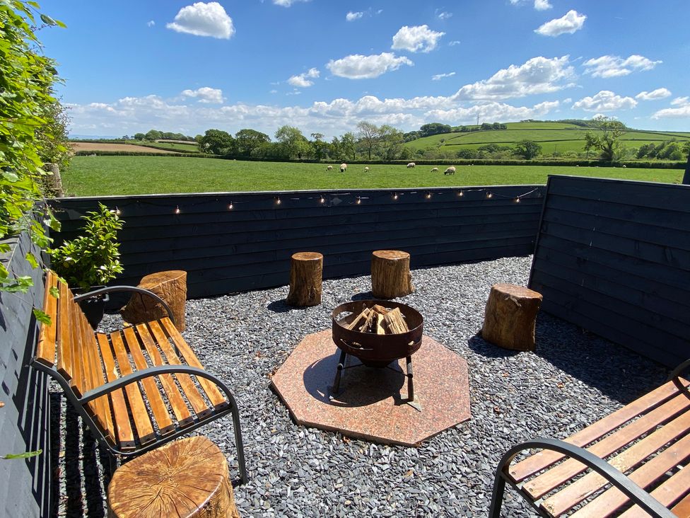 An outdoor seating area with wooden benches tree stump stools a fire pit and a view of green fields and hills at Ashlea in Launceston