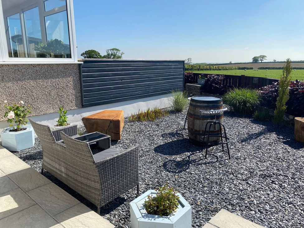 An outdoor patio area with a wicker loveseat, a wooden stump, potted plants, a wooden barrel table, and a metal bar stool at Ashlea in Launceston
