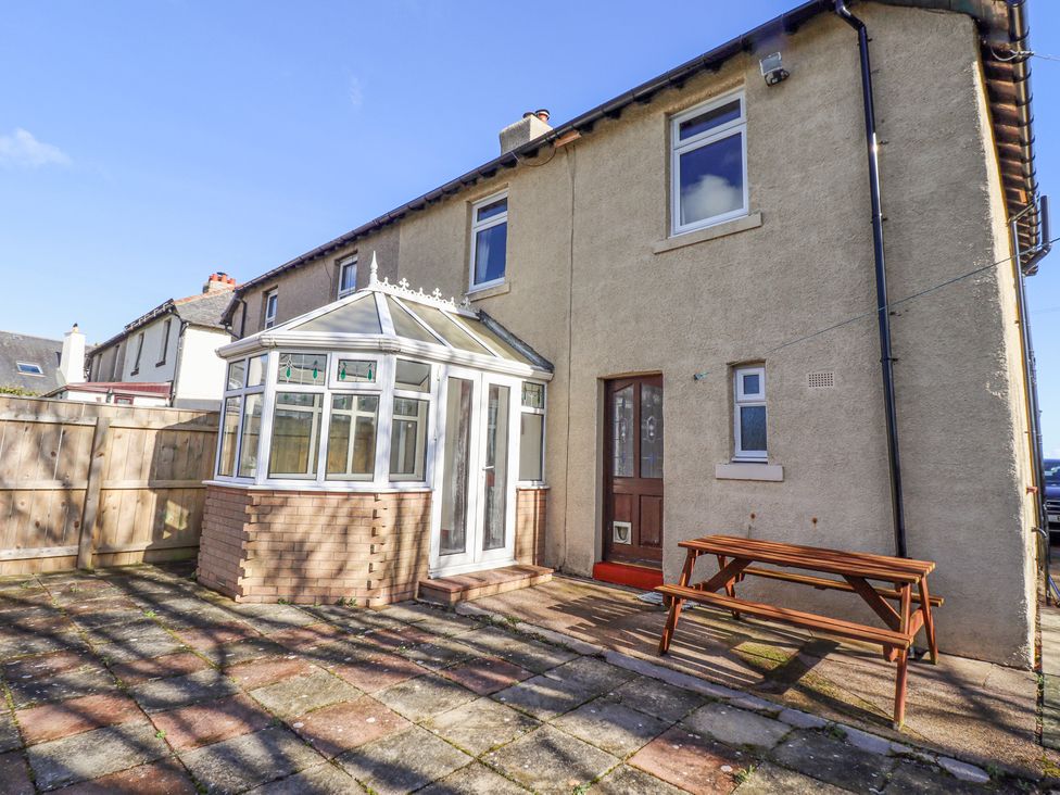 An outdoor patio area with a conservatory attached to a house and a wooden picnic table at St Marys Cottages No1 in Low Newton-by-the-Sea