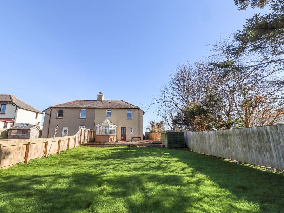A backyard with green grass fenced by wooden panels and a house with a conservatory at St Marys Cottages No1 in Low Newton-by-the-Sea