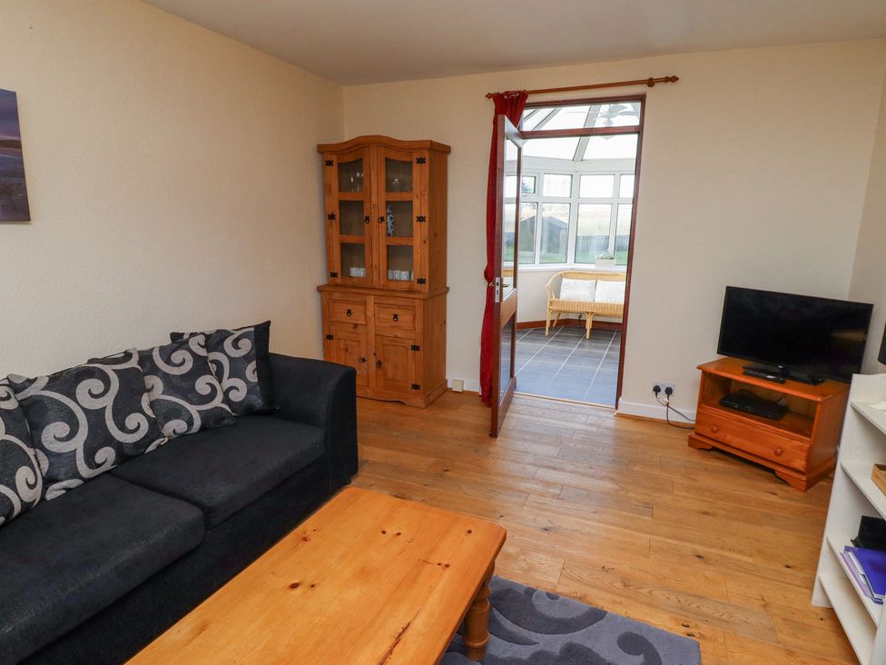 A living room with a black sofa and patterned cushions a wooden cabinet a television on a wooden stand and a wooden coffee table at St Marys Cottages No1 Low Newton-by-the-Sea