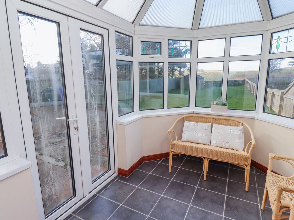 A conservatory with a glass door, wicker furniture, and a planter on the windowsill at St Marys Cottages No1 in Low Newton-by-the-Sea