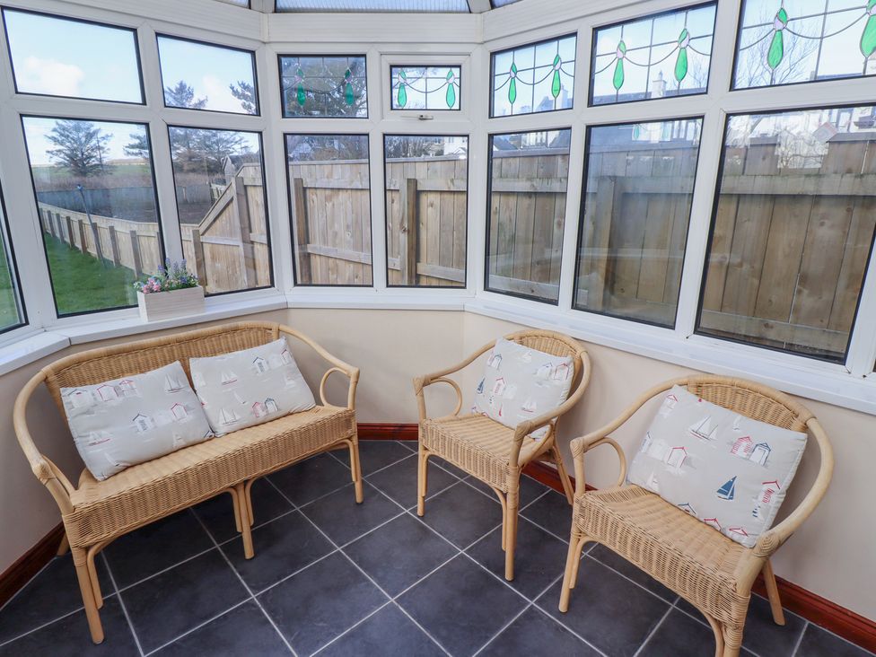 A sunroom with wicker chairs and a bench with cushions and stained glass windows at St Marys Cottages No1 in Low Newton-by-the-Sea
