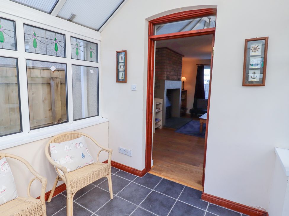 A sunroom with wicker chairs and nautical cushions next to windows and a doorway leading to a living room at St Marys Cottages No1 in Low Newton-by-the-Sea