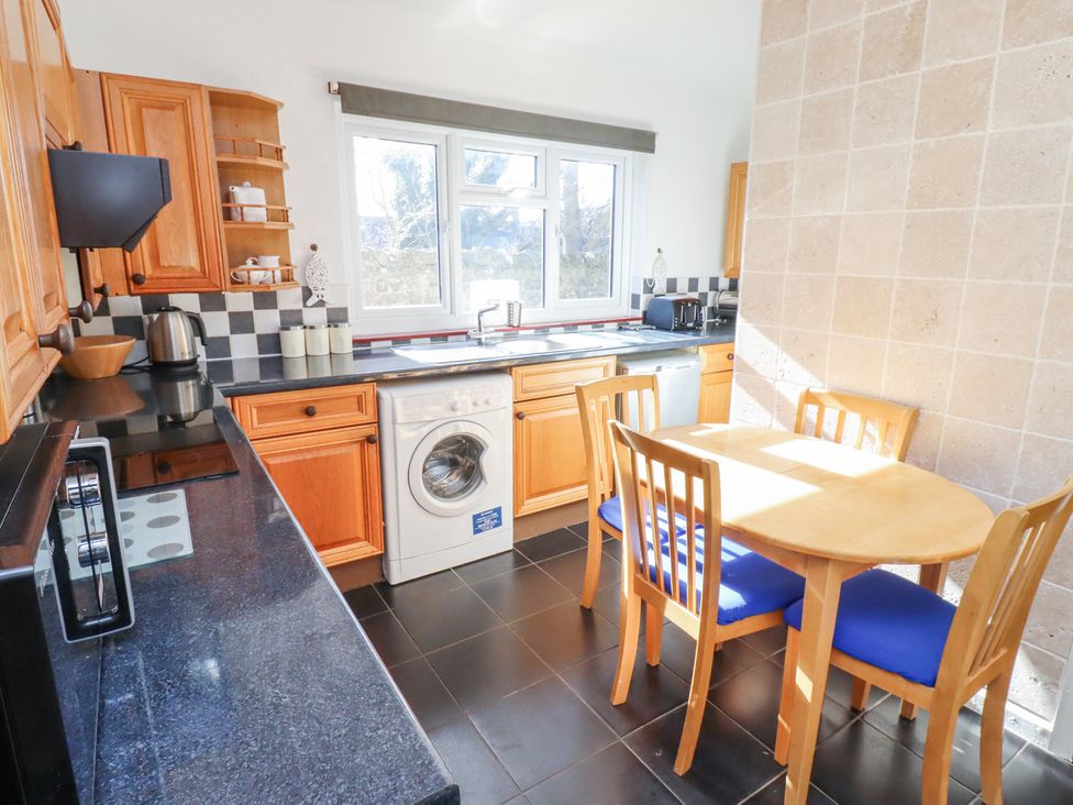 A kitchen with wooden cabinets a washing machine a dining table and chairs at St Marys Cottages No1 in Low Newton-by-the-Sea