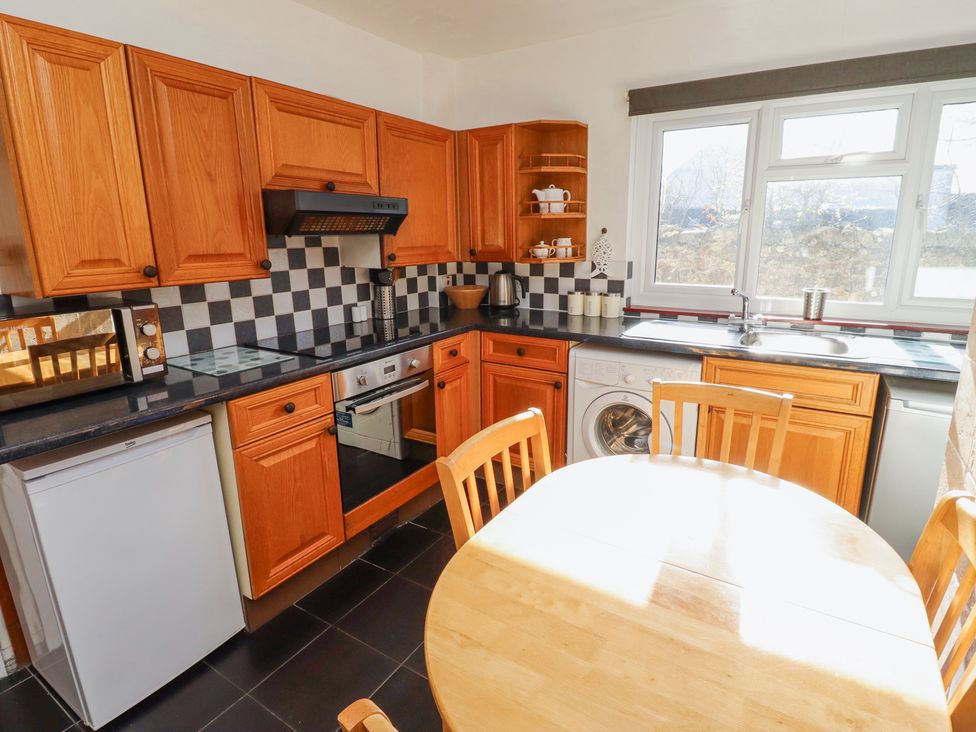 A kitchen with wooden cabinets a round wooden table and chairs a refrigerator a washing machine and a window at St Marys Cottages No1 in Low Newton-by-the-Sea