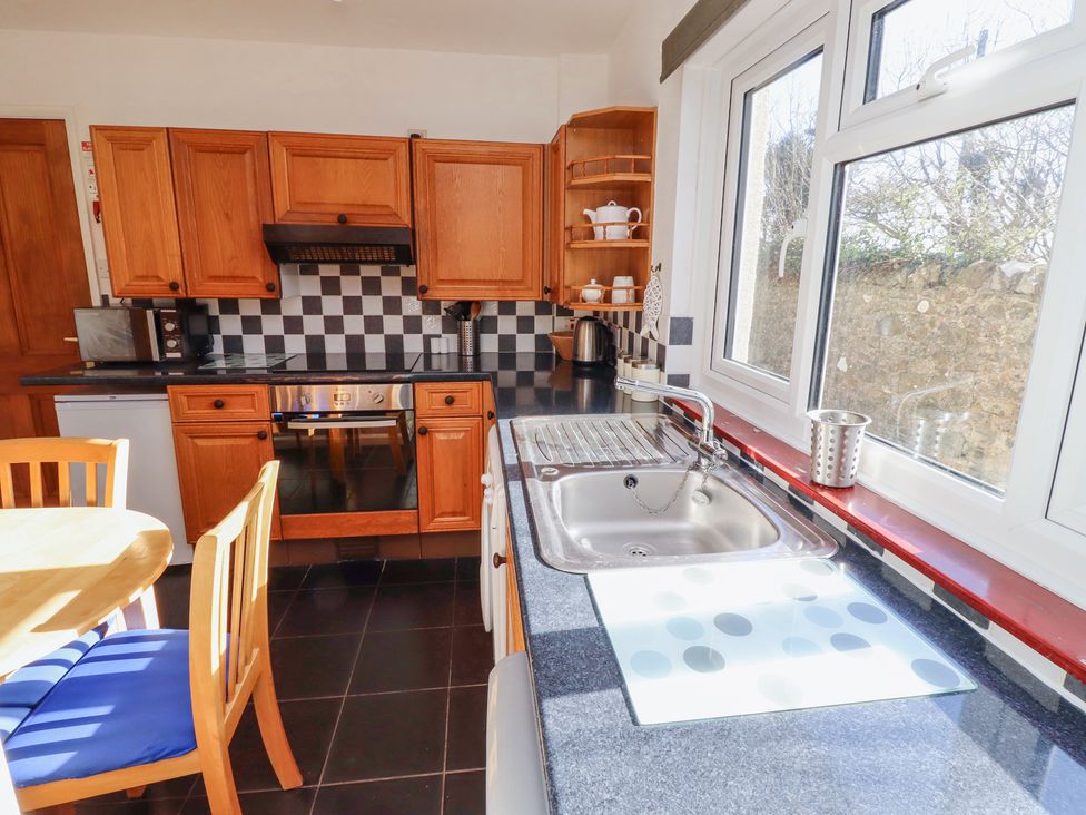 A kitchen with wooden cabinets a dining table with blue cushioned chairs and a window over a sink at St Marys Cottages No1 in Low Newton-by-the-Sea