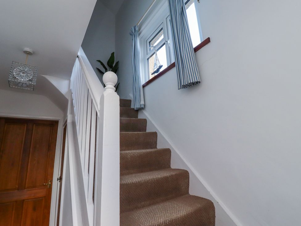 A carpeted staircase with white banister and a window with blue striped curtains at St Marys Cottages No1 in Low Newton-by-the-Sea