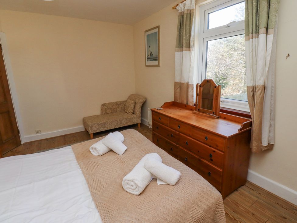 A bedroom with a bed with towels on it a wooden dresser with a mirror a chaise lounge and a window with curtains at St Marys Cottages No1 in Low Newton-by-the-Sea