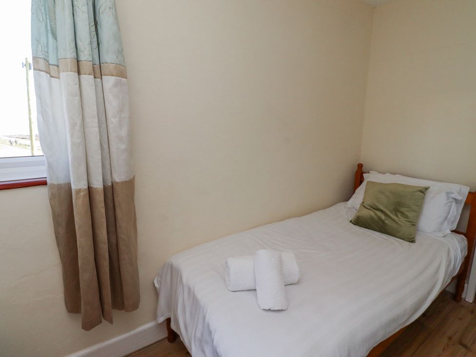 A single bed with white linens and a green pillow next to a window with beige and light blue curtains at St Marys Cottages No1 in Low Newton-by-the-Sea