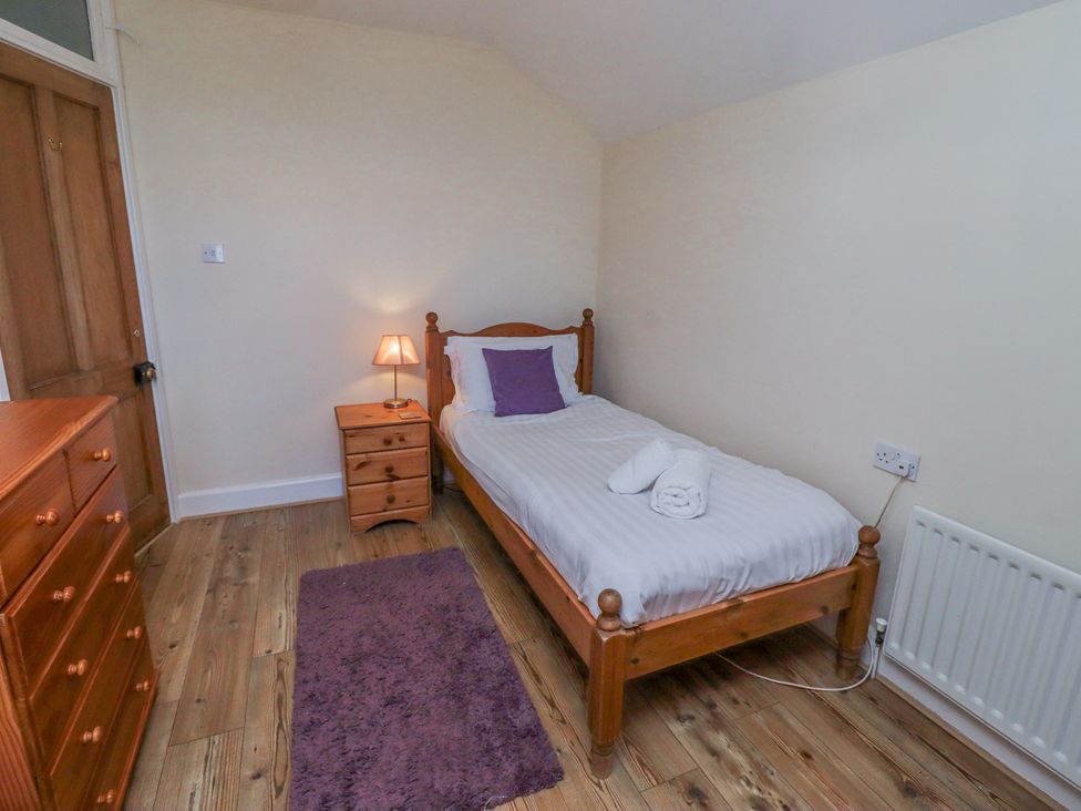 A bedroom with a single wooden bed a bedside table with a lamp a wooden chest of drawers and a purple rug at St Marys Cottages No1 in Low Newton-by-the-Sea