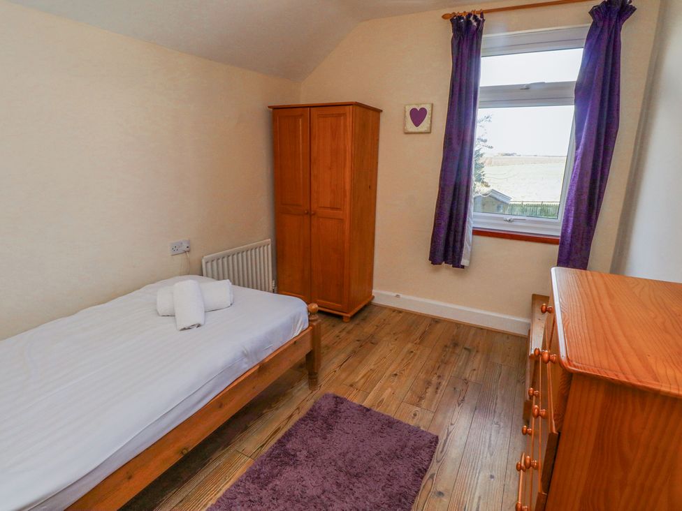 A bedroom with a single bed a wooden wardrobe a chest of drawers and a window with purple curtains at St Marys Cottages No1 in Low Newton-by-the-Sea