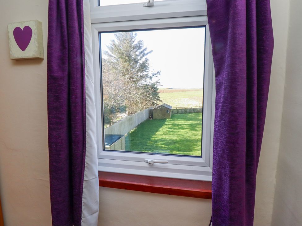 A window with purple curtains showing a green backyard with a shed and trees at St Marys Cottages No1 in Low Newton-by-the-Sea