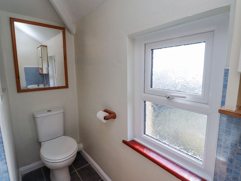 A small bathroom with a toilet a mirror above it and a window with frosted glass at St Marys Cottages No1 in Low Newton-by-the-Sea