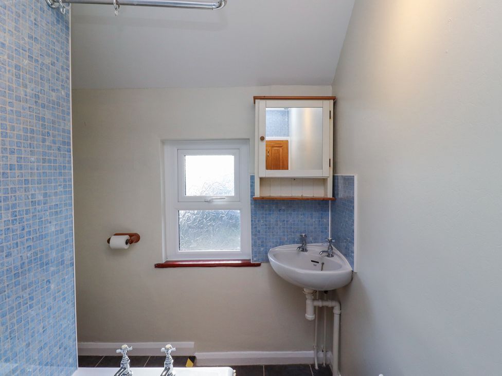 A bathroom with a corner sink and mirror cabinet above it and a frosted window at St Marys Cottages No1 Low Newton-by-the-Sea