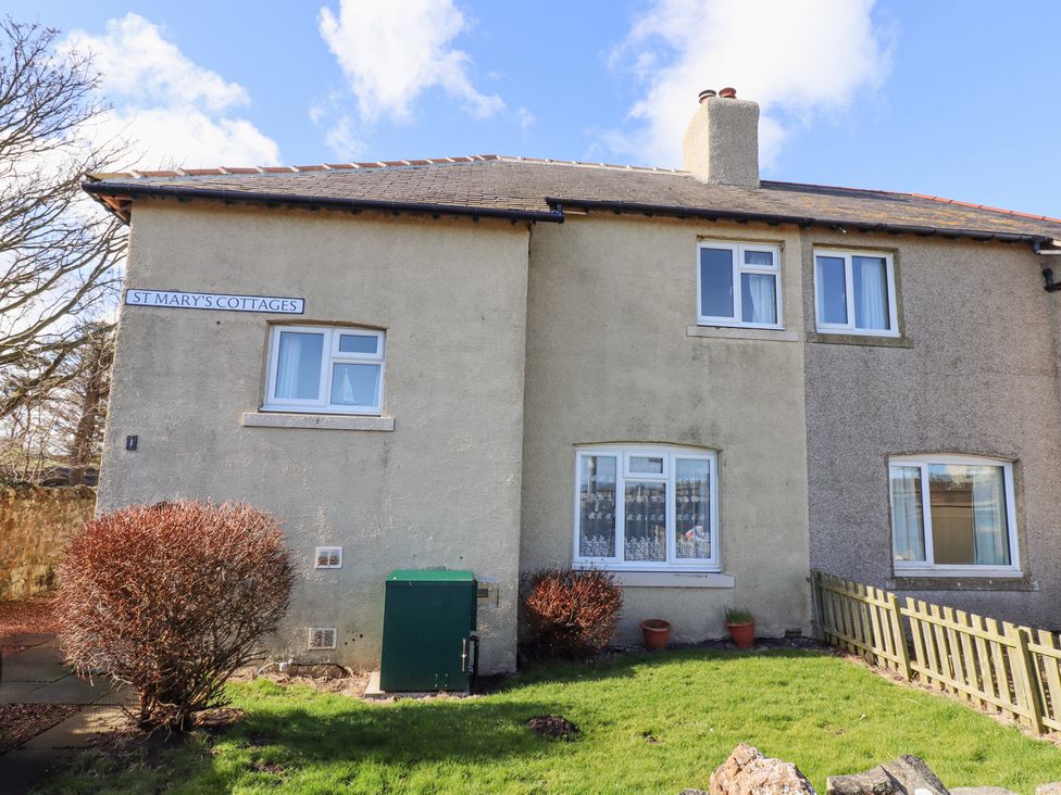 Exterior of a two story stone cottage with windows bushes and a green utility box at St Marys Cottages in Low Newton-by-the-Sea
