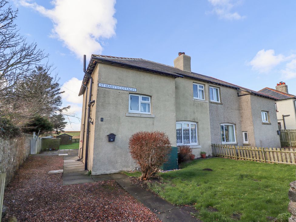 A two-story semi-detached house with a small front garden and gravel driveway at St Marys Cottages in Low Newton-by-the-Sea
