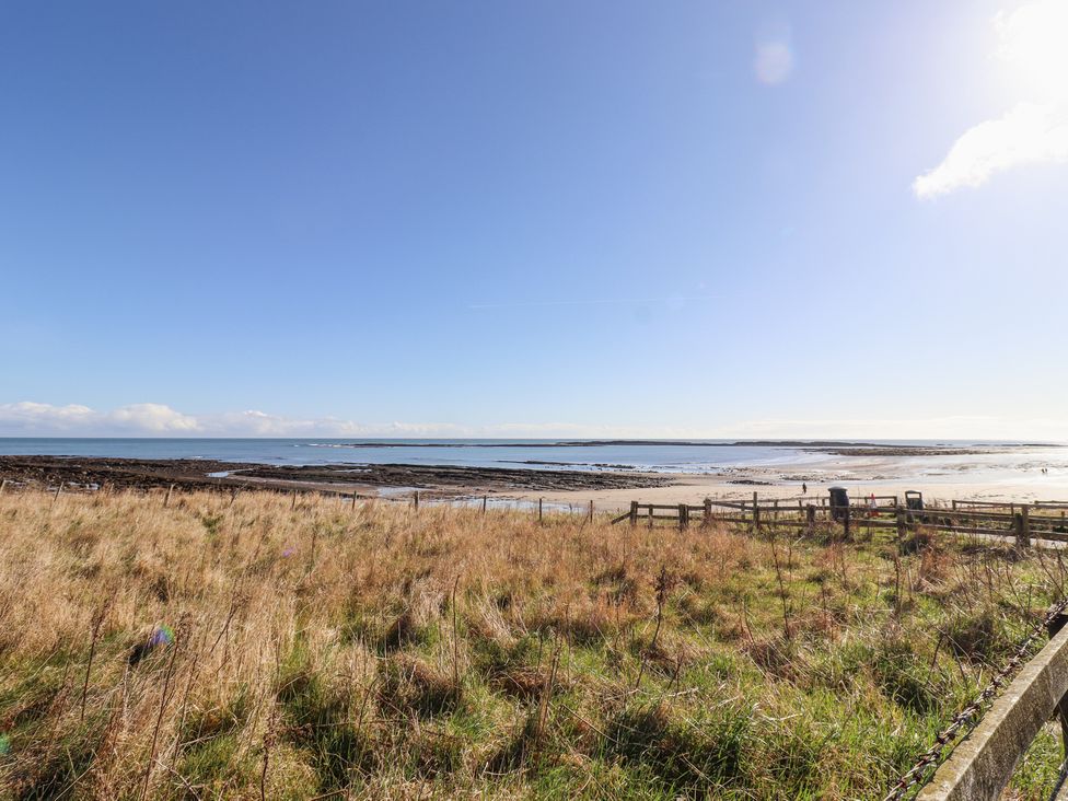 A grassy field overlooking a beach with a wooden fence and the sea beyond at St Marys Cottages No1 in Low Newton-by-the-Sea