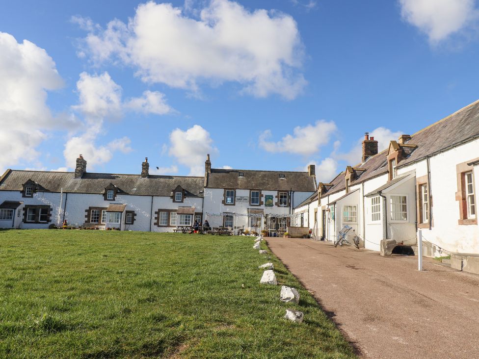 A row of white cottages with a grassy area and pathway under a blue sky at St Marys Cottages No1 in Low Newton-by-the-Sea