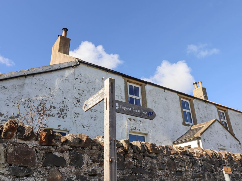 A signpost for England Coast Path next to a stone wall and white building under a blue sky at St Marys Cottages No1 in Low Newton-by-the-Sea