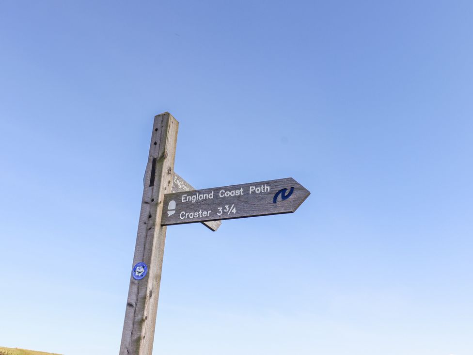 A wooden signpost showing directions for England Coast Path and Craster against a blue sky at St Marys Cottages No1 in Low Newton-by-the-Sea