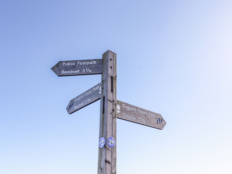A wooden signpost with directions for public footpath and England coast path at St Marys Cottages No1 in Low Newton-by-the-Sea