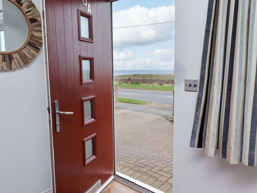A hallway with a red door and a mirror at Farne Cottage Beadnell