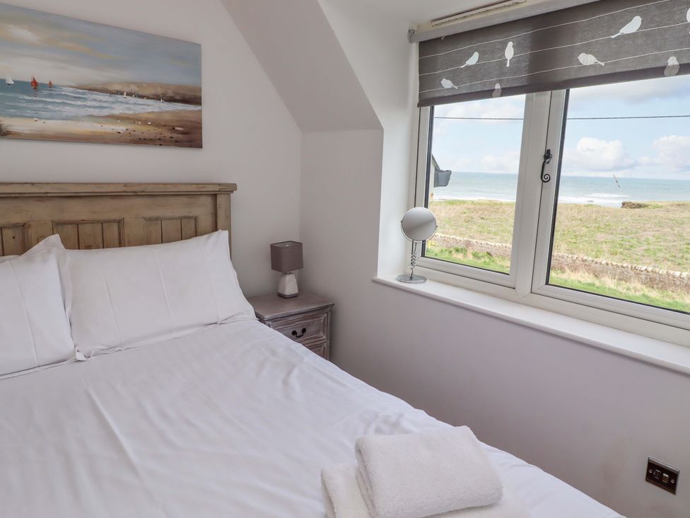 A bedroom with a bed and window showing the sea at Farne Cottage Beadnell