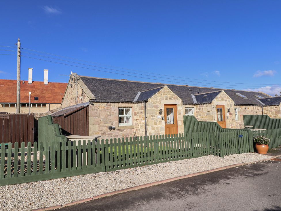 A cottage with wooden fence and gravel in front at Avocet Cottage - Lucker Steadings, Lucker