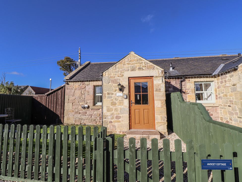 A cottage with a wooden door and fenced garden at Avocet Cottage - Lucker Steadings, Lucker