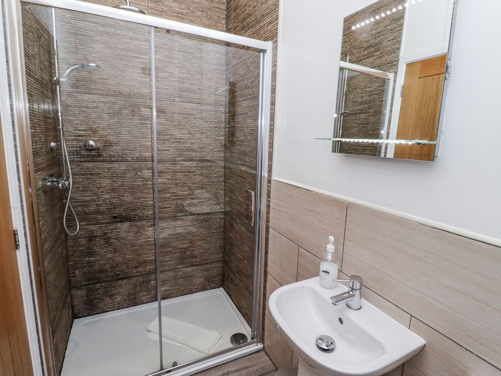 A shower with glass doors and a sink at Avocet Cottage - Lucker Steadings, Lucker