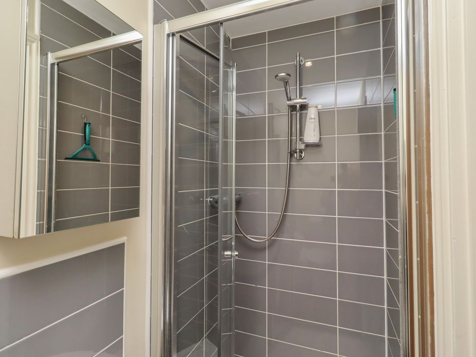 A shower with a mirror and wall tiles at The Beach Hut in Beadnell