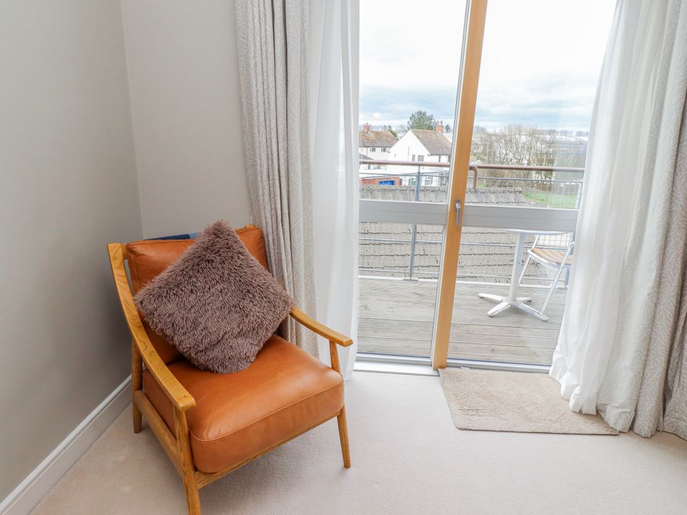 A living room with a chair and door leading to the balcony at Cuddy's Holm in Seahouses