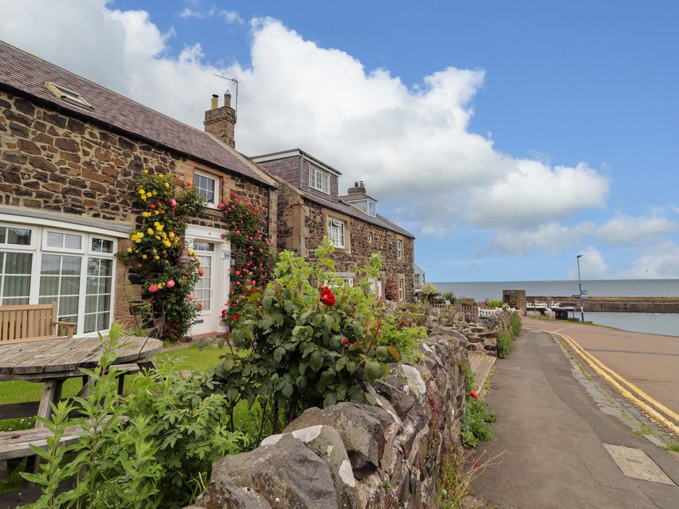 An outdoor area with stone walls and flowers at Coble Cottage in Craster