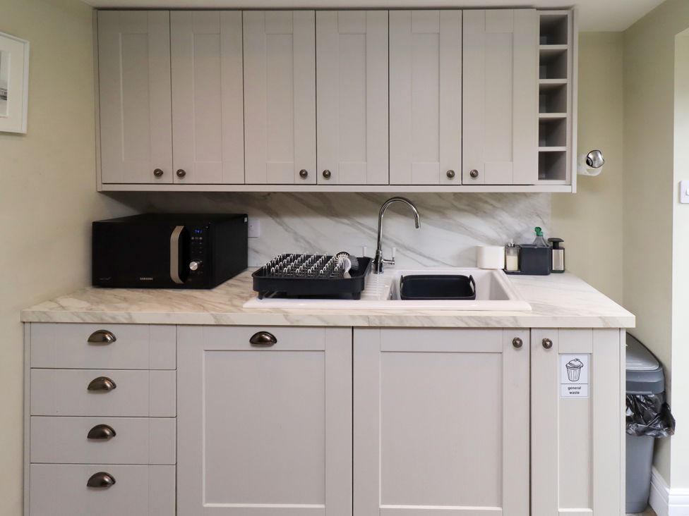 A kitchen with cabinets, sink, microwave, and dish rack at Coble Cottage, Craster