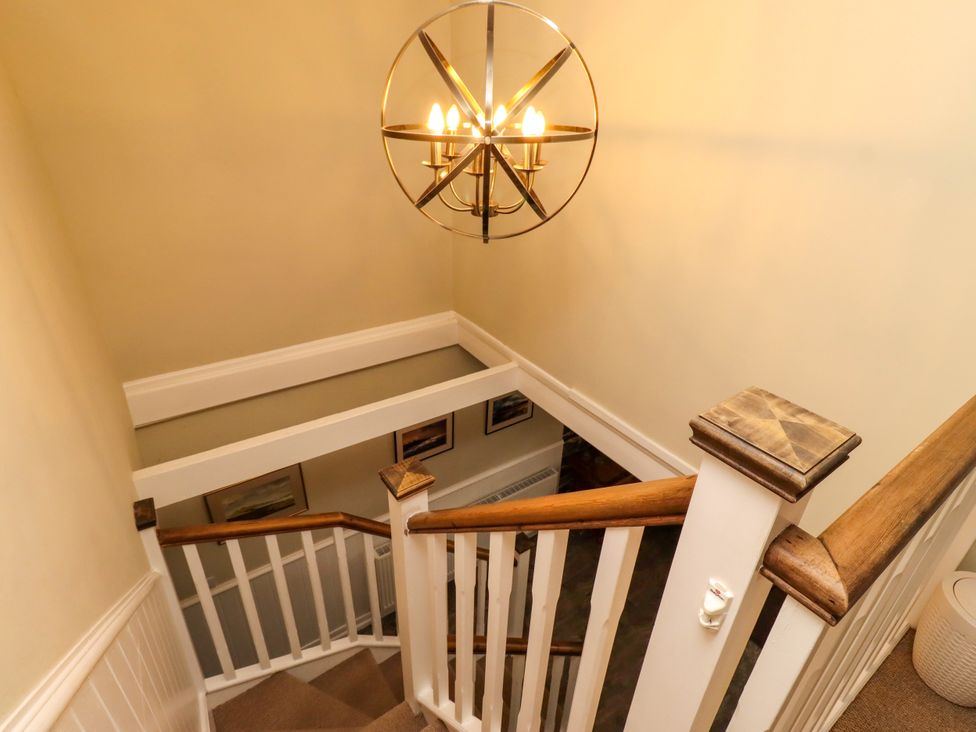A staircase with a chandelier and framed pictures at Coble Cottage in Craster