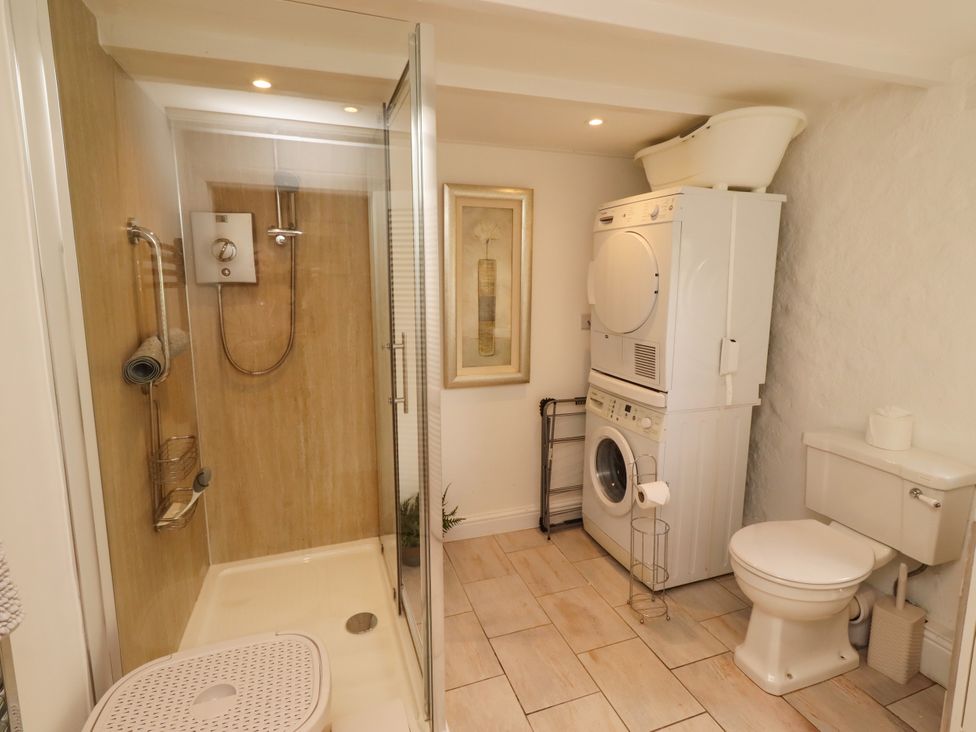 A bathroom with a shower, toilet, and laundry appliances at Coble Cottage Craster