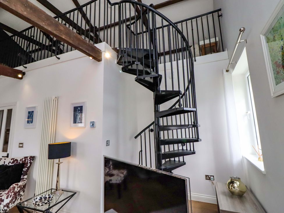 A living room with a spiral staircase and a television at Treetops, Alnwick
