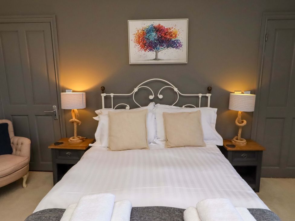 A bedroom with a bed, bedside tables, lamps, and artwork at Treetops, Alnwick