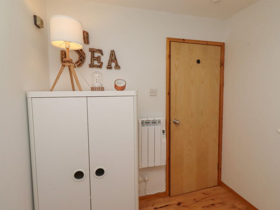 A hallway with a cupboard, lamp, clock, and door at Links View in Embleton