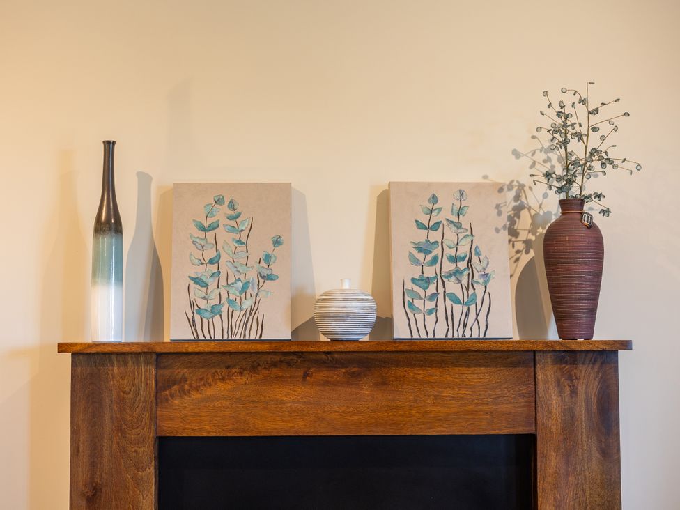 A living room with a wooden mantel displaying vases and artwork at Plumtree Cottage in Alnmouth
