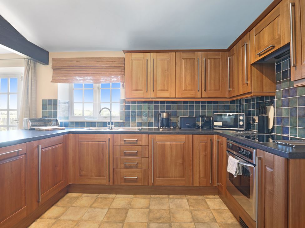 A kitchen with wooden cabinets and appliances at Plumtree Cottage in Alnmouth